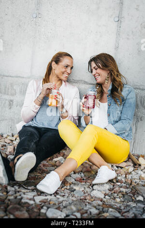 Two female friends drinking smoothies outdoors having fun Stock Photo