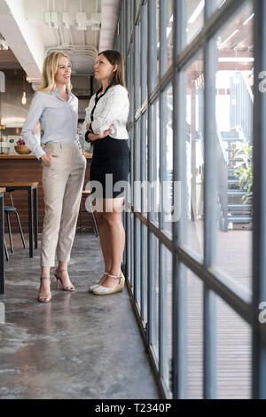 Two female colleagues talking in cafe in front of windows Stock Photo