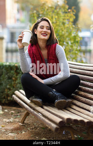 Portrait of smiling young woman relaxing with coffee to go on a bench Stock Photo