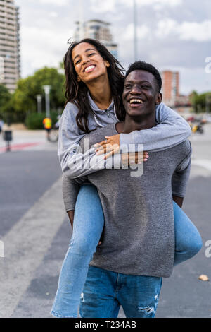 Young man carrying his girlfriend piggyback in the street Stock Photo