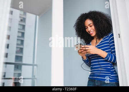 Portrait of smiling young woman using smartphone and earphones at home Stock Photo