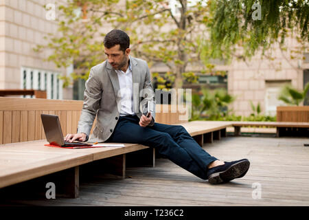 Businessman sitting on a bench using laptop Stock Photo