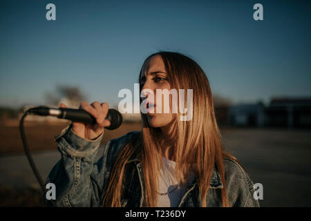 Young woman singing with a microphone outdoors Stock Photo