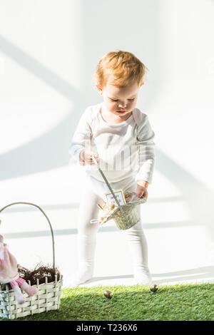 adorable child holding straw basket while standing on green grass in sunlight Stock Photo