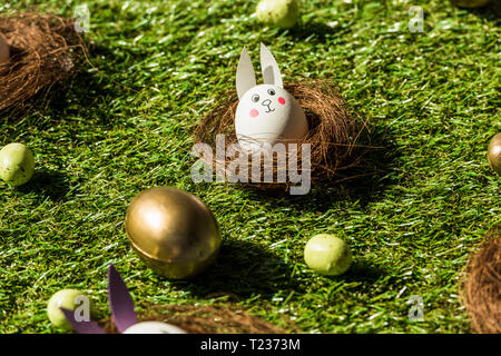 Easter eggs and chicken egg with funny rabbit face and paper ears on green grass Stock Photo