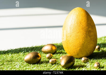 yellow ostrich egg and golden Easter eggs on green grass surface Stock Photo
