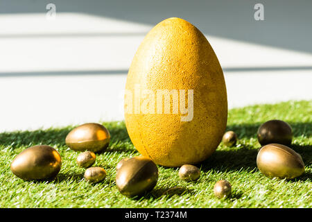 yellow ostrich egg and golden chicken and quail eggs on green grass surface Stock Photo