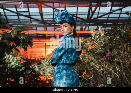 Gorgeous young woman in blue dress in turban in orangery Stock Photo