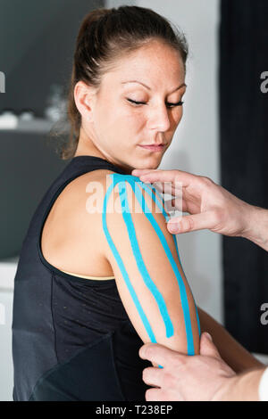 Physical therapist placing kinesio tape on patient's shoulder. Stock Photo