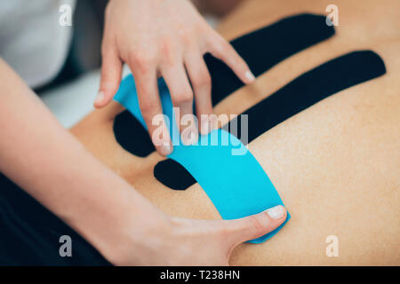 Physical therapist placing kinesio tape on patient's knee. Stock Photo