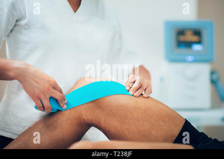 Physical therapist placing kinesio tape on patient's knee. Stock Photo