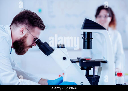 Young male researcher looking at samples under microscope. Stock Photo