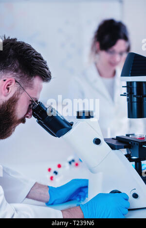 Young male researcher looking at samples under microscope in the laboratory. Stock Photo