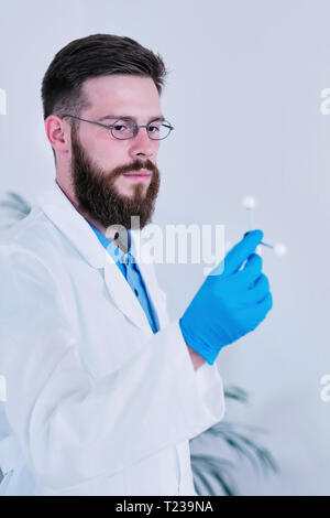 Portrait of male researcher wearing white coat in laboratory, holding molecular structure. Stock Photo