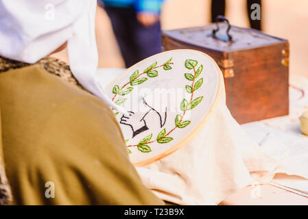 Young woman seamstress sewing a simple drawing, disguised as medieval in a traditional craft children's exhibition. Stock Photo
