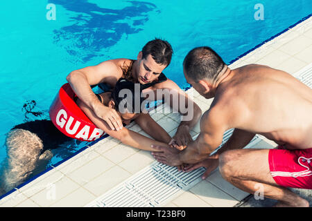 Lifeguards with woman on poolside. Stock Photo