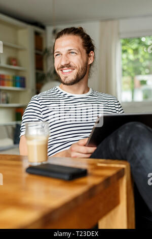 Young man with a bun sitting at home, using digital tablet Stock Photo