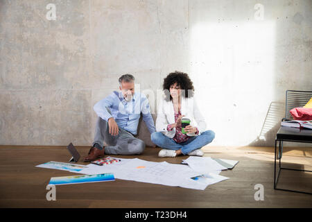 Businessman and businesswoman sitting on the floor in a loft discussing documents Stock Photo