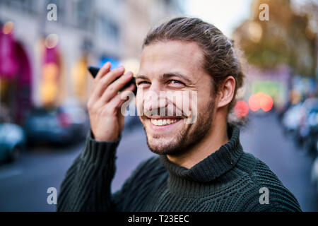 Portrait of laughing young man using smartphone on the street in the evening Stock Photo