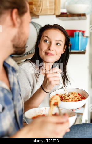 Happy couple sitting in kitchen, eating spaghetti Stock Photo