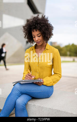 Woman sitting on bench taking notes Stock Photo