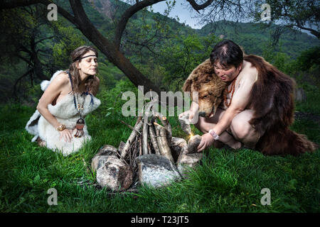 Cave people dressed in animal skin making fire in the forest Stock Photo