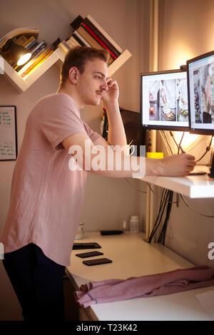 one young man, 20-29 years old, looking to two computer monitors, while working on a computer in his room, at his home. using standing desk. Stock Photo