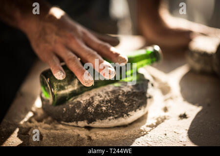 Man preparing black burger buns in kitchen, rolling dough with a bottle Stock Photo