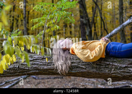 Girl lying on tree trunk in autumnal forest relaxing Stock Photo