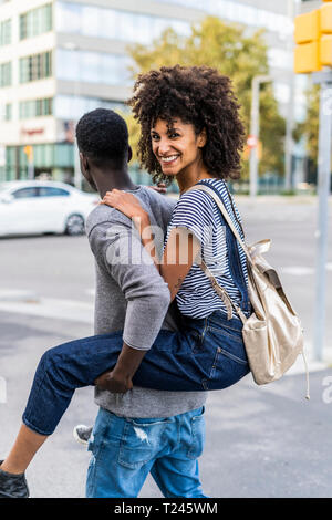 Young man carrying his girlfriend piggyback in the street Stock Photo