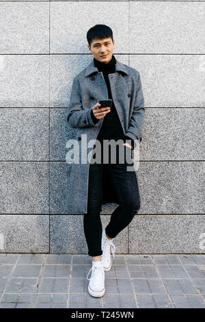 Portrait of stylish young man with mobile phone leaning against wall Stock Photo