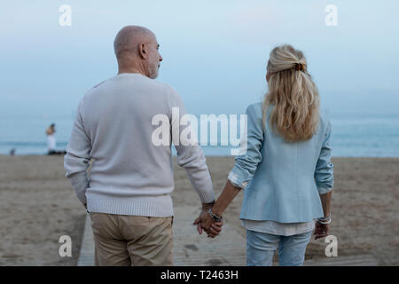 Spain, Barcelona, rear view of senior couple walking hand in hand on the beach at dusk Stock Photo