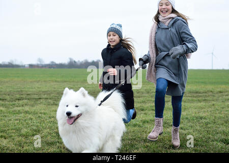 Two girls running on a meadow with dog having fun Stock Photo
