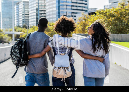 Three friends exploring the city, walking down the street, arm in arm Stock Photo