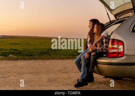 Two happy sisters sitting at opened tail watching sunset together Stock Photo