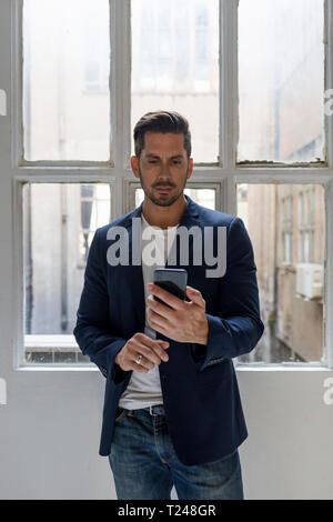 Businessman standing in a loft at the window using cell phone Stock Photo