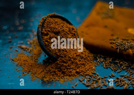 Close up of powdered cumin or zeera or jeera with raw cumin on wooden surface in a clay bowl on a cloth or napkin. Stock Photo