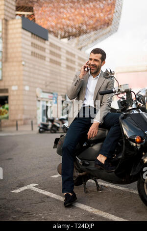 Smiling businessman on motorscooter talking on cell phone Stock Photo