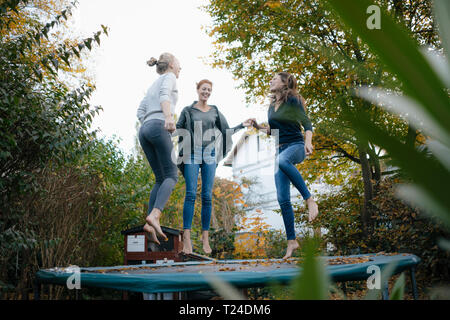 Happy mother with two teenage girls jumping on trampoline in garden in autumn Stock Photo