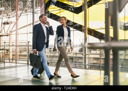Businessman on cell phone and businesswoman walking at the airport Stock Photo
