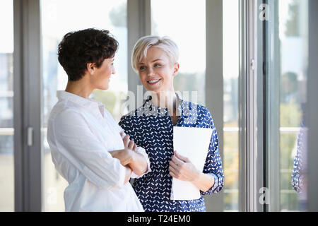 Two smiling businesswomen talking at the window in office Stock Photo