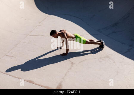 Barechested muscular man doing push-ups in a skatepark Stock Photo