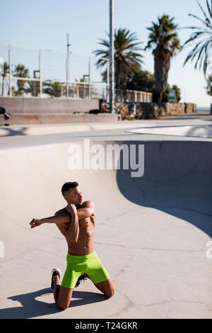 Barechested muscular man doing stretching exercise in a skatepark Stock Photo