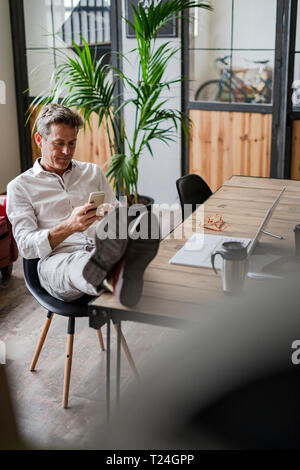 Businessman sitting with feet on desk using cell phone Stock Photo