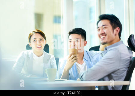 three young asian entrepreneurs sitting at desk discussing business. Stock Photo