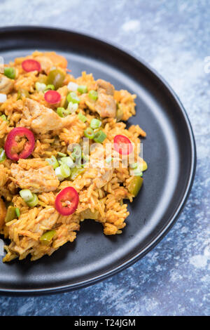 Close up of an African chicken jollof rice dish. Orange spiced African rice with red chillies and chicken on a dark plate and grey background. Stock Photo