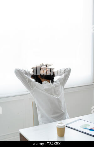 Young man relxing in office, with hands behind head Stock Photo