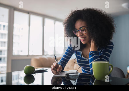 Smiling young woman taking notes at home Stock Photo