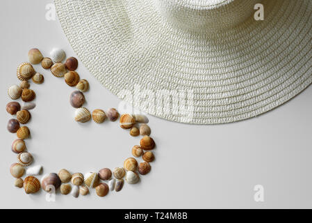 Beach style set-up created from summer straw hat and symbol of love - heart made from seashells. Stock Photo
