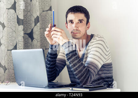 Portrait of young man In casual wear on the job working on laptop looking at with thoughtful face Stock Photo